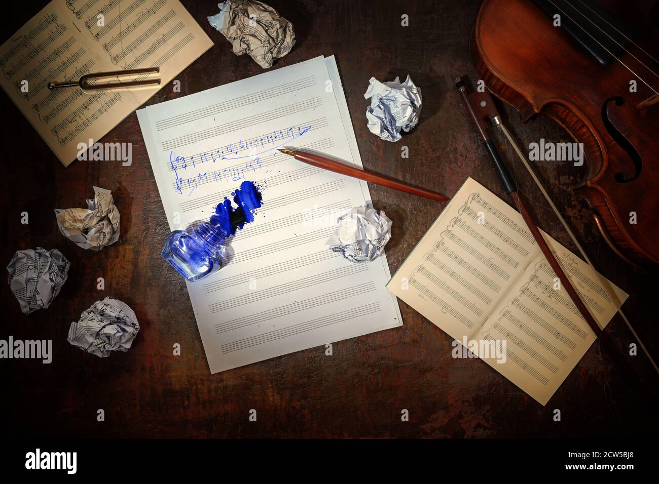 Violin, plain and crumpled sheet of music, handwritten beginning of a musical composition and a overturned inkwell on a dark brown table, workplace of Stock Photo