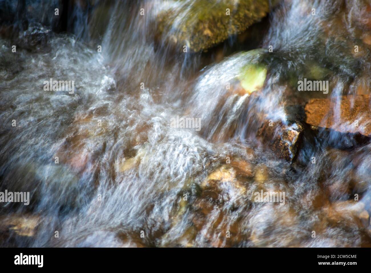 Abstract long -exposure woodland stream cascading over colorful stones and leaves. Stock Photo