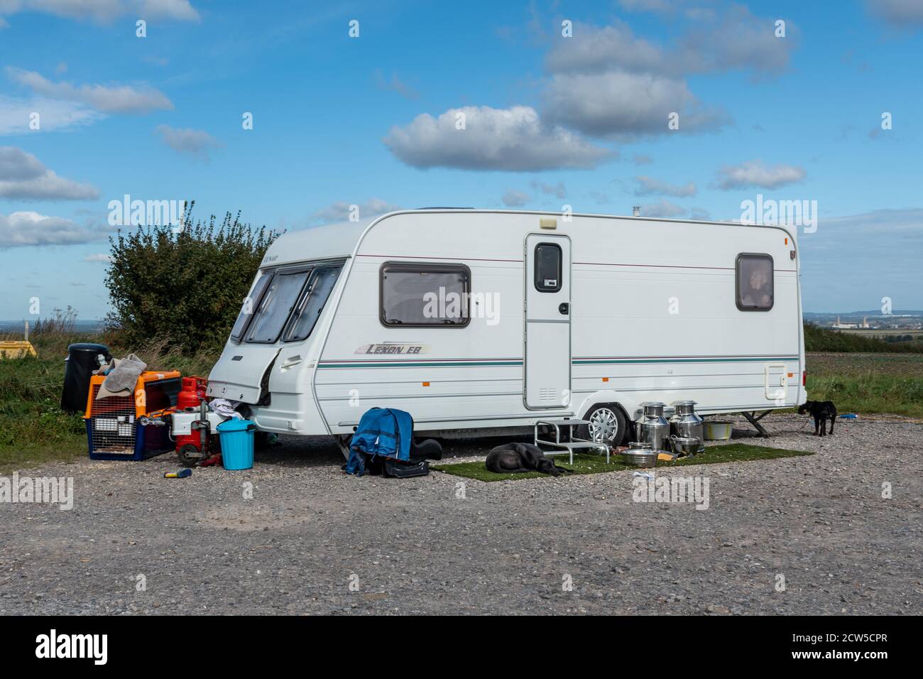 Caravan belonging to travellers parked illegally in a countryside car park with dogs and belongings outside, UK Stock Photo