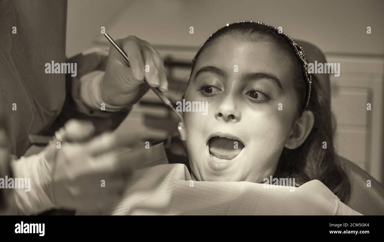 Young caucasian female with dentist in white latex gloves check condition of her teeth. baby girl in blue dental chair Stock Photo