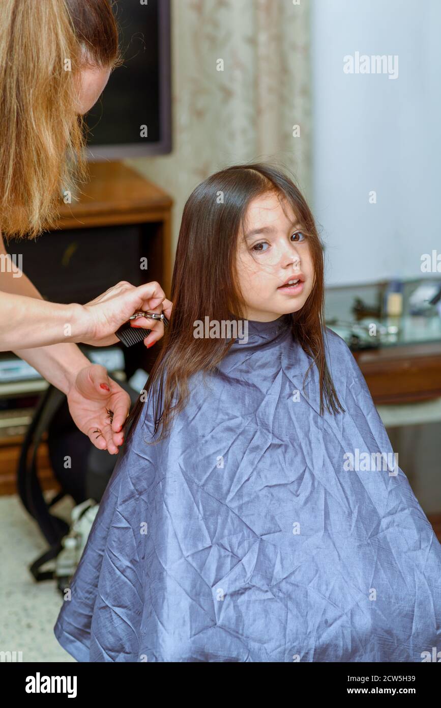 Portrait Of A Young Girl Getting Her Hair Cut In Home Womans Hand With