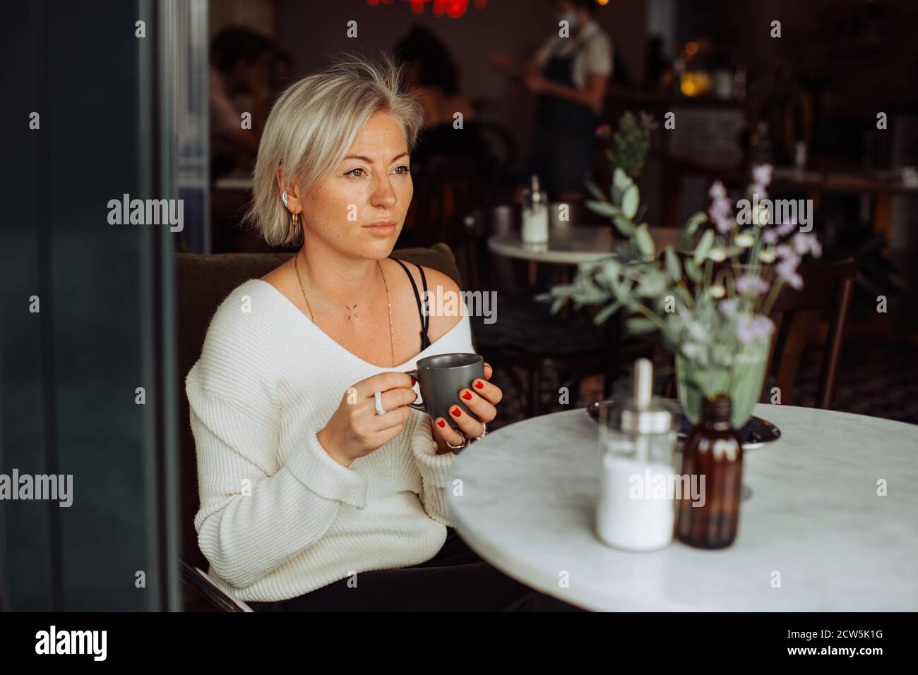 Blond woman holding cup of tea while sitting alone at table in cafe Stock Photo