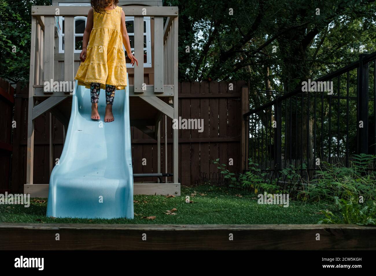 Little girl in yellow dress standing on blue slide Stock Photo