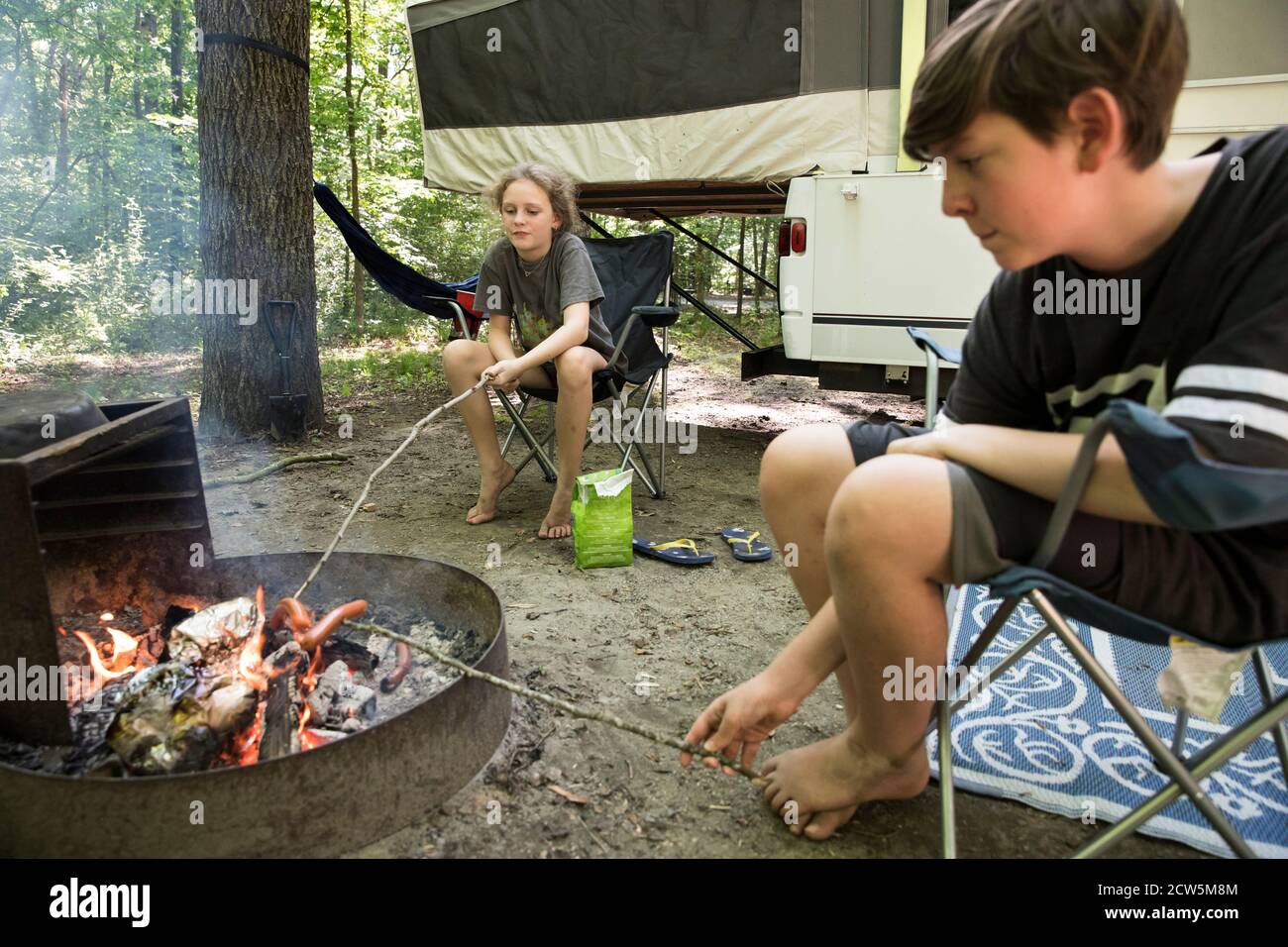Tween Siblings on Family Camping Trip Roast Hot Dogs Over Campfire Stock Photo