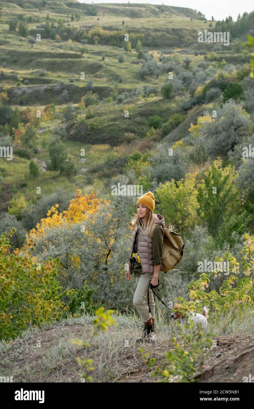 Young female backpacker in warm casualwear with her pet moving down footpath Stock Photo