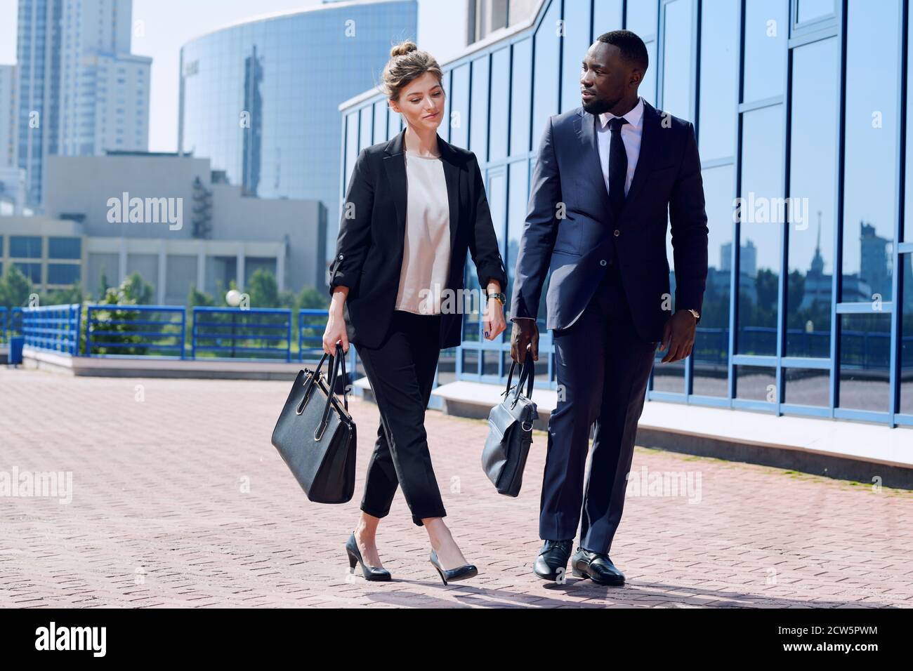 Young intercultural business partners in formalwear moving down sidewalk Stock Photo