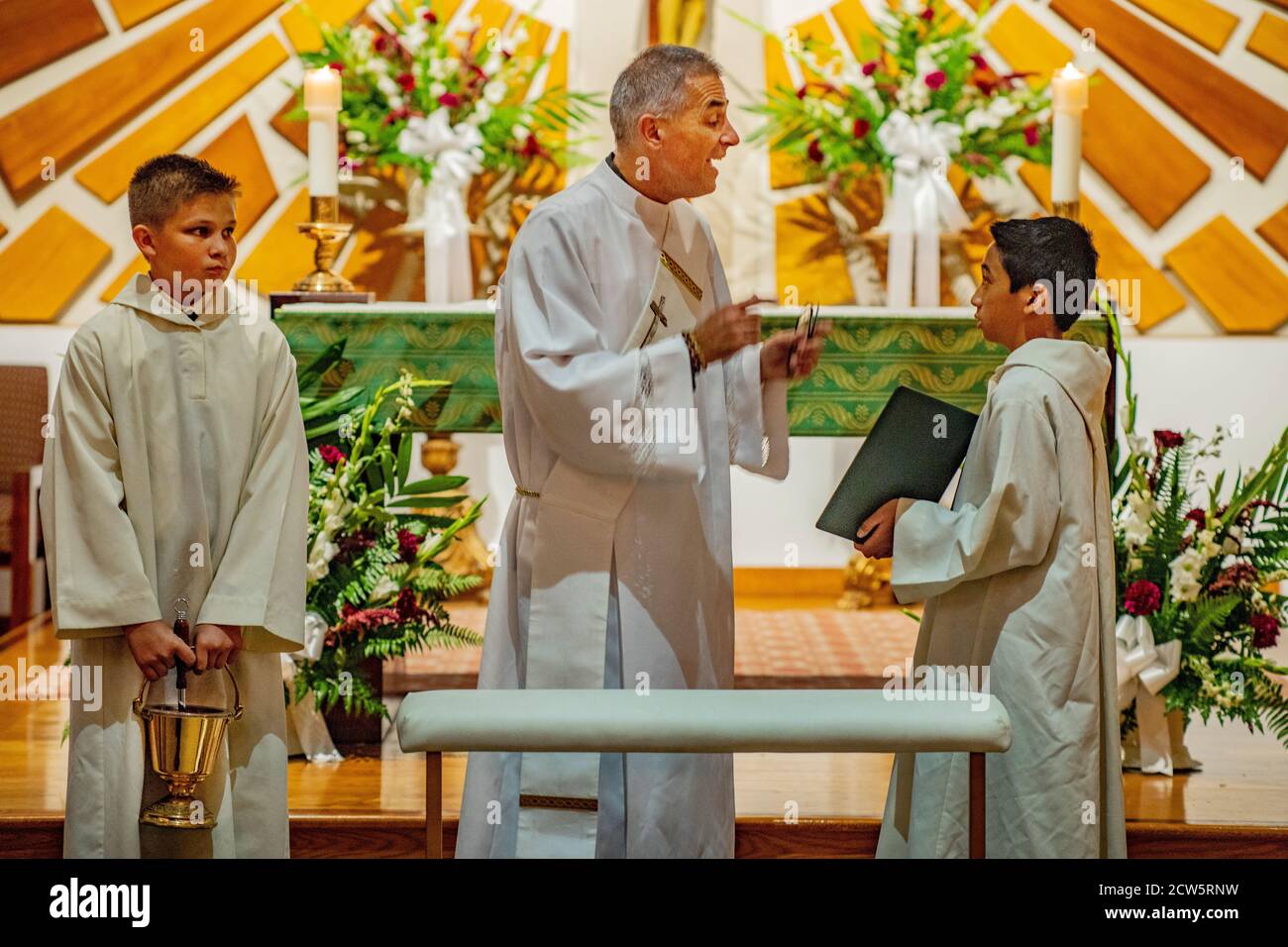 At a Southern California Catholic church, a robed deacon with a picture sash converses with two young boy altar assistant before celebrating a mass. Stock Photo