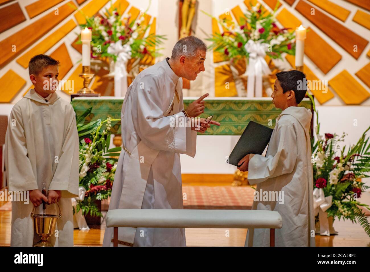 At a Southern California Catholic church, a robed deacon with a picture sash converses with two young boy altar assistant before celebrating a mass. Stock Photo