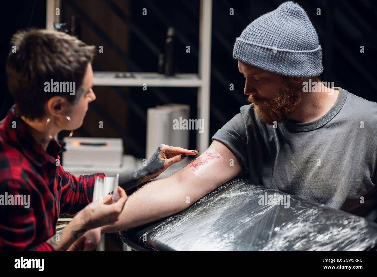 A tattoo artist bandages the young man's hand with a thin layer of