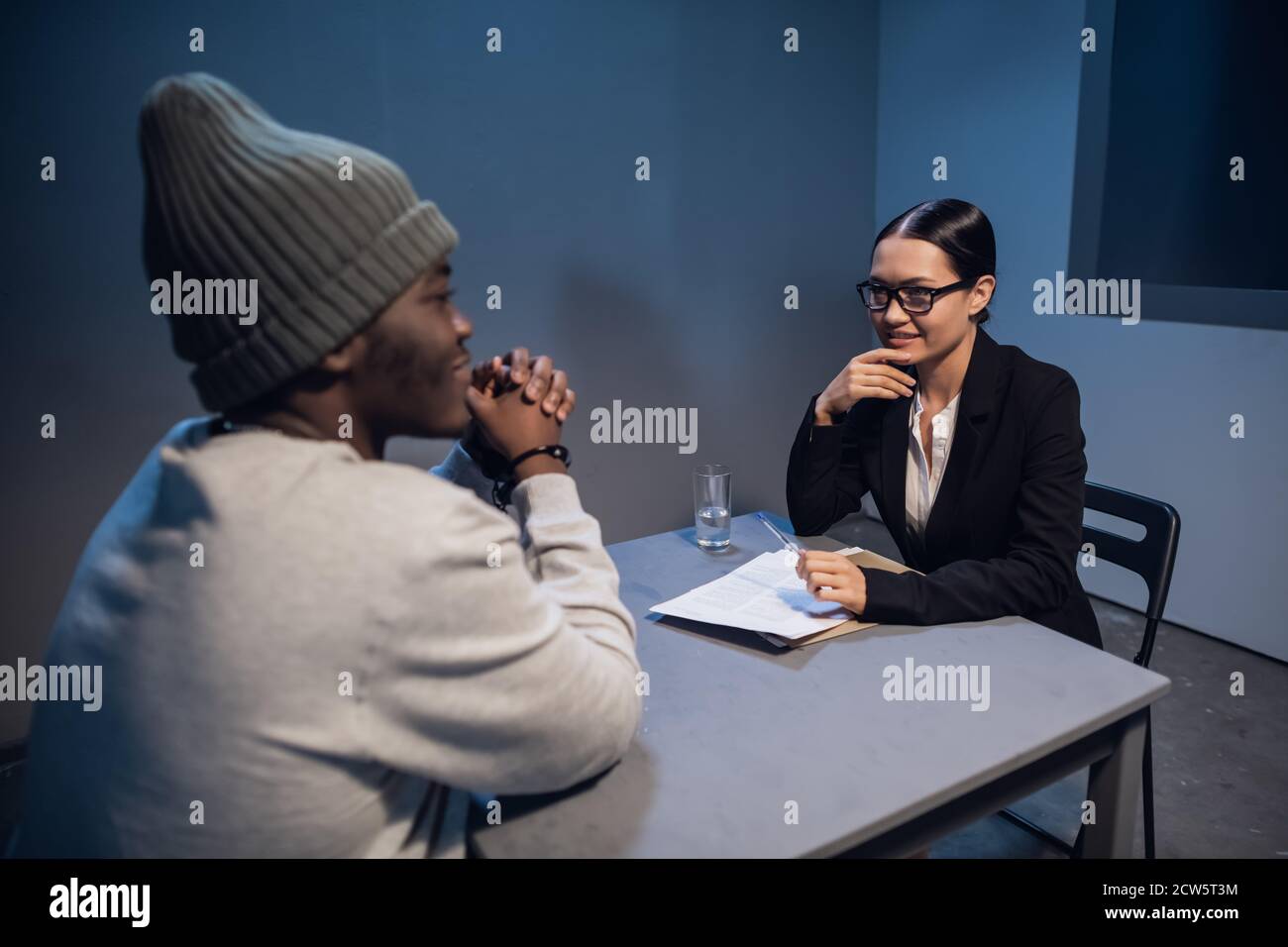 Beautiful girl investigator interrogates a young black man accused of drug distribution. Stock Photo