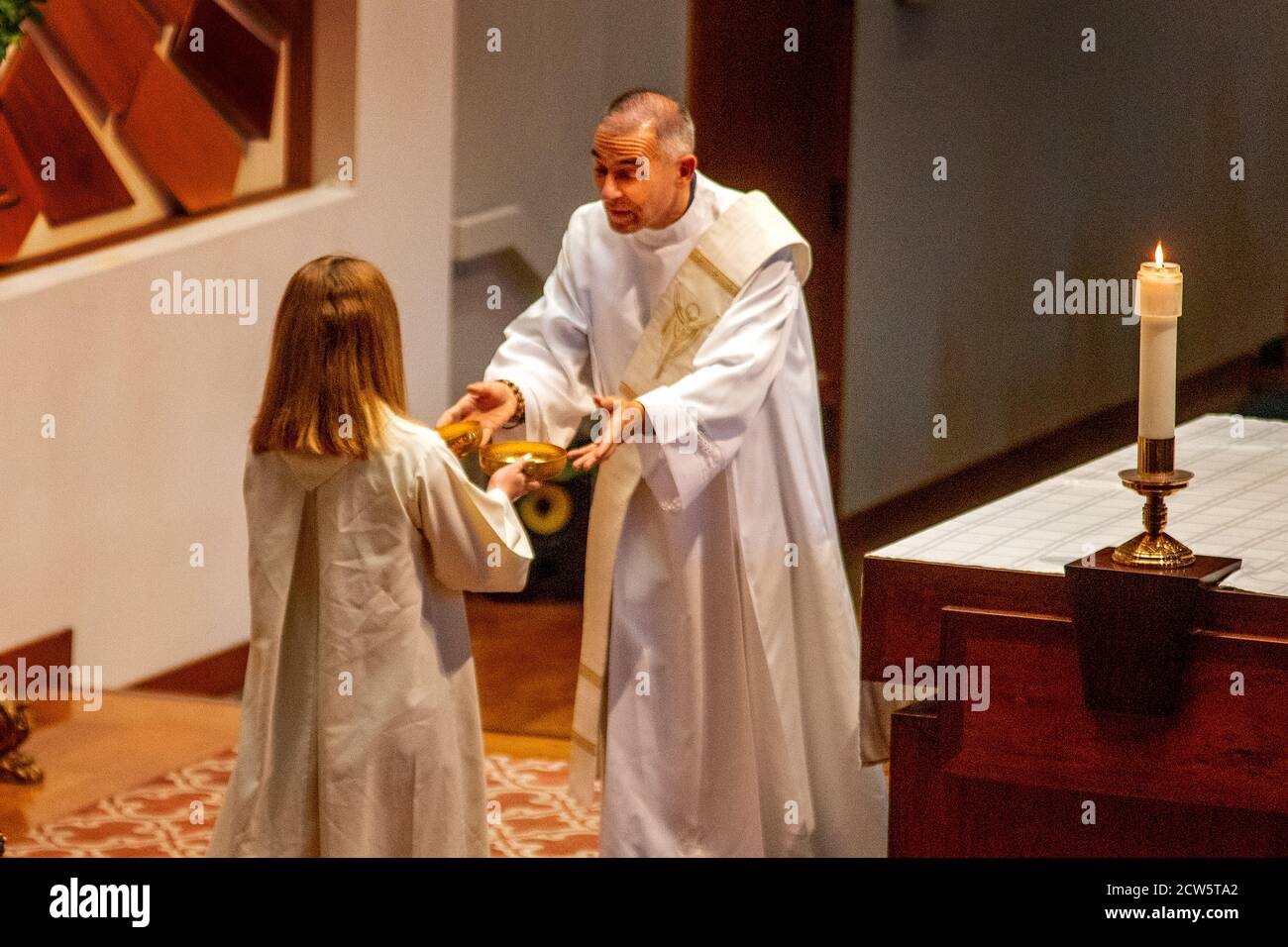 A robed deacon receives bowls of holy water from a female assistant while participating in mass at the altar of a Southern California Catholic church. Stock Photo