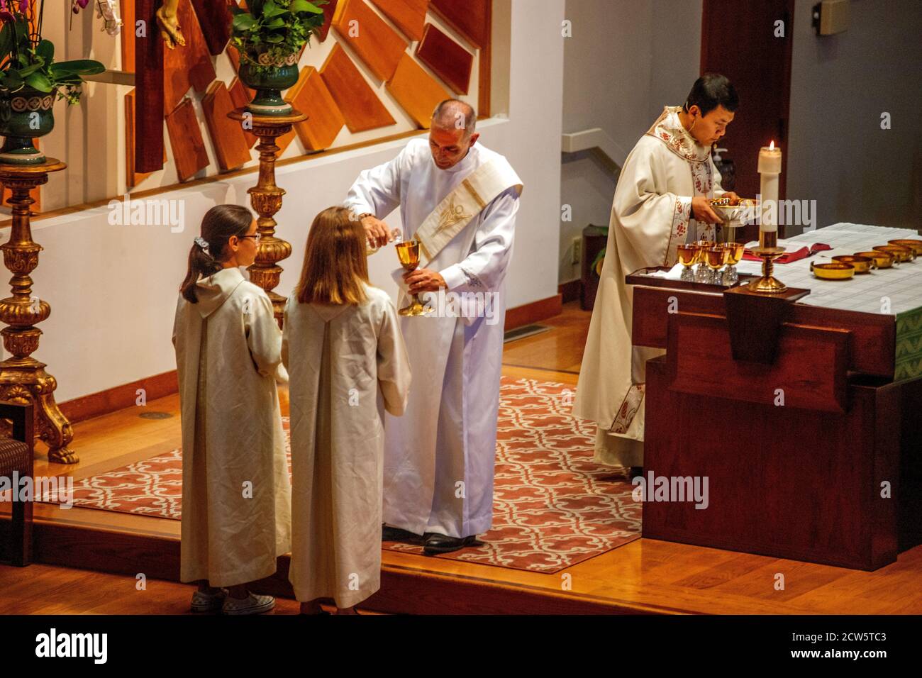 A robed deacon pours a goblet of sacramental wine received from a female assistant while participating in mass at the altar of a Southern California C Stock Photo