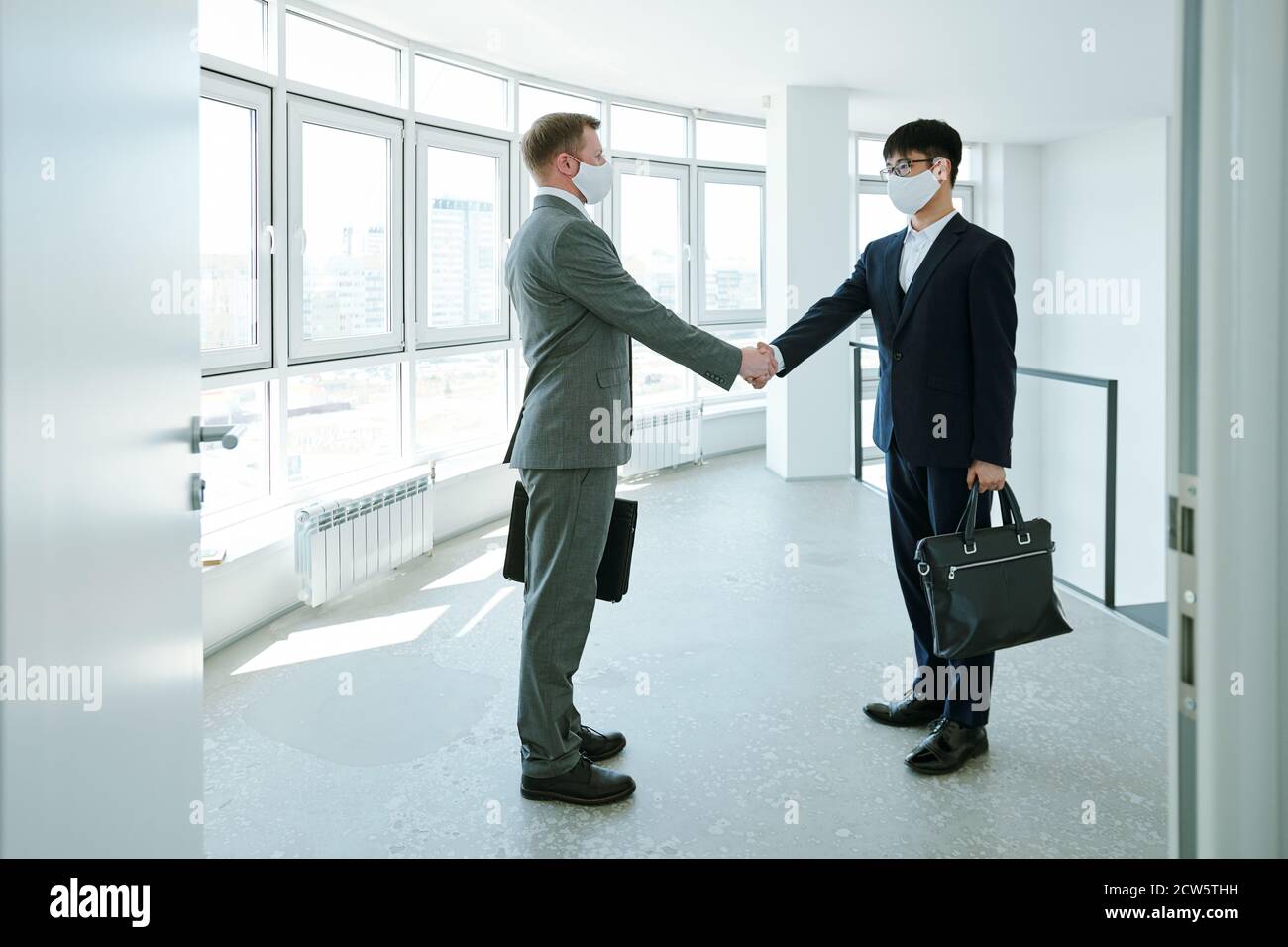 Two young intercultural successful businessmen shaking hands in corridor Stock Photo