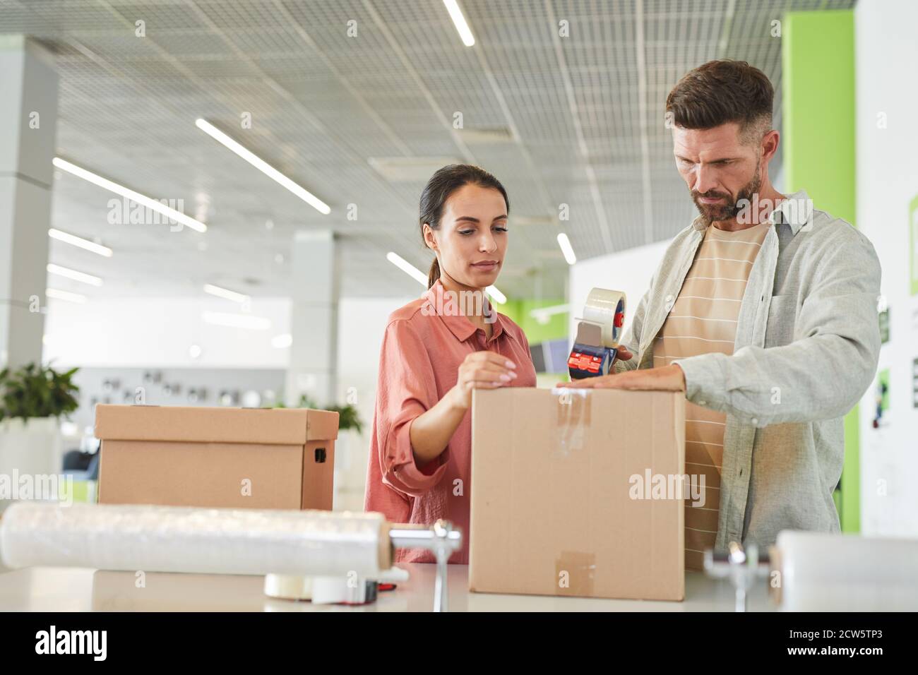 Waist up portrait of modern adult couple packing cardboard boxes with tape gun in storage facility or shipping service, copy space Stock Photo