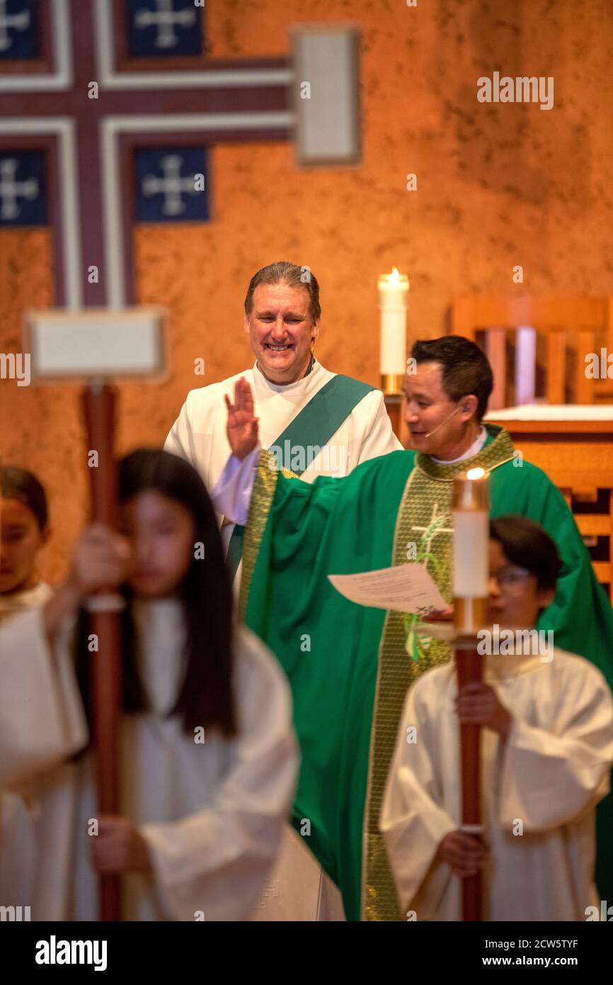 A robed deacon and an Asian American priest celebrate mass at the altar of a Southern California Catholic church. Stock Photo