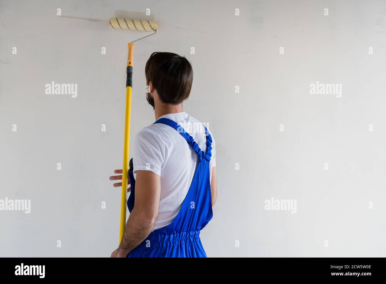 Repairer in work clothes paints the wall white with a roller Stock Photo