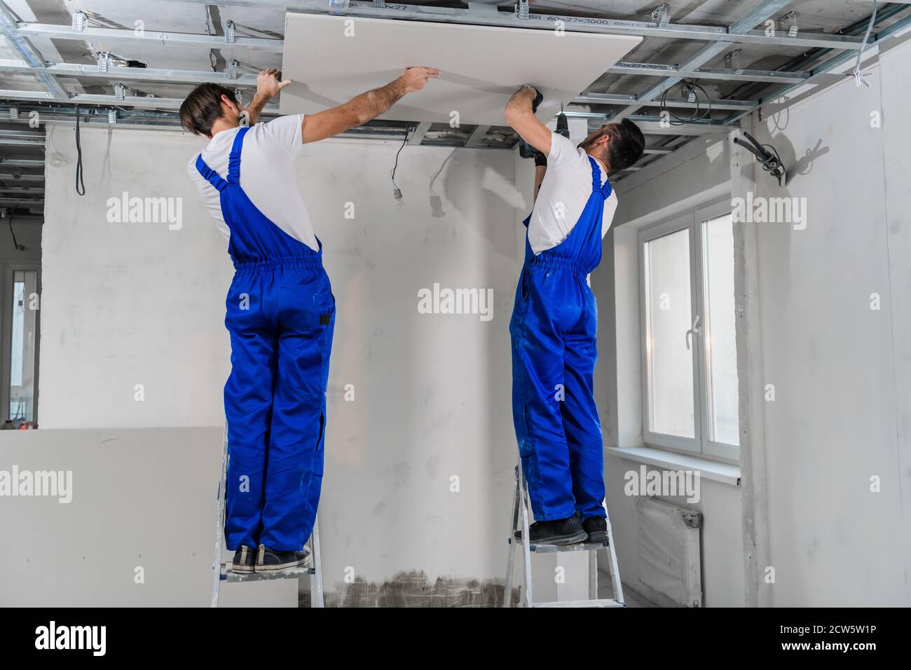 Men in blue overalls stand on a ladder and make a ceiling Stock Photo