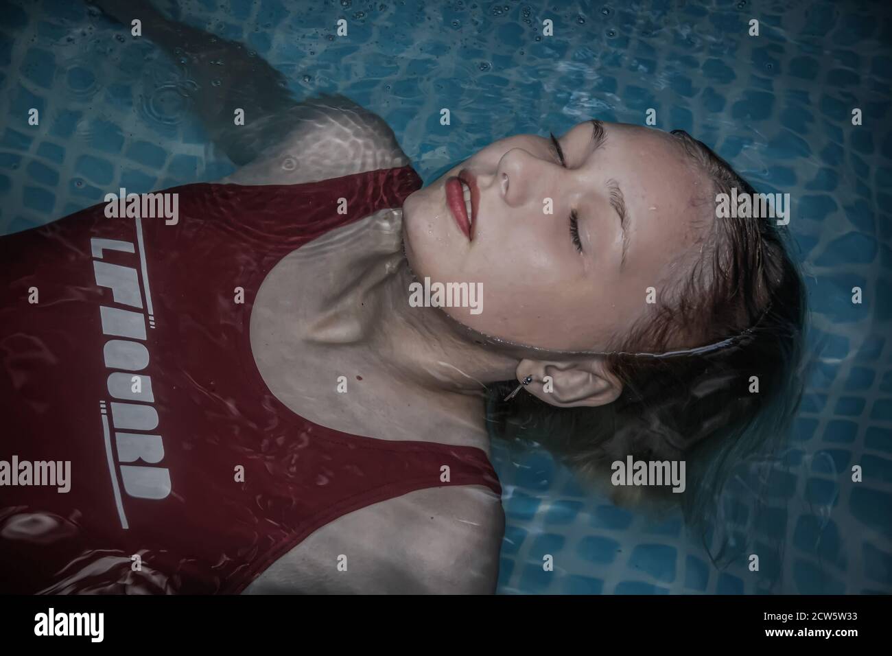 A Young And Beautiful Girl In A Red Bathing Suit Is Lying In The Pool Almost Completely 