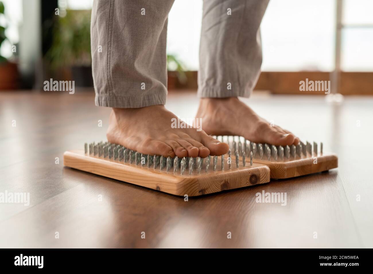 Legs of young barefoot man in sportspants standing on yoga pads with nails Stock Photo