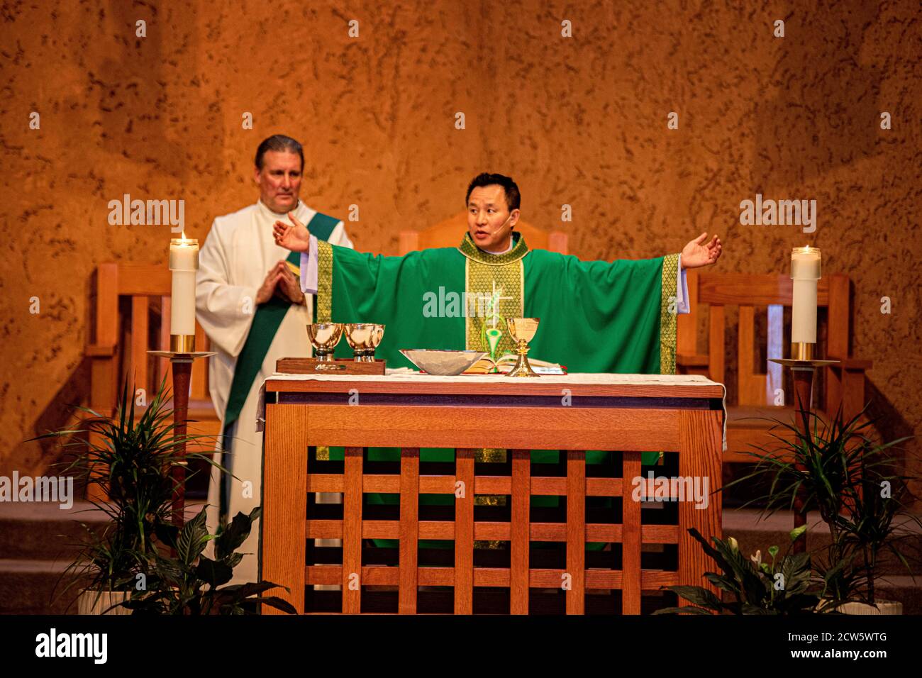 A robed deacon and an Asian American priest celebrate mass at the altar of a Southern California Catholic church. Note goblets for sacramental wine. Stock Photo