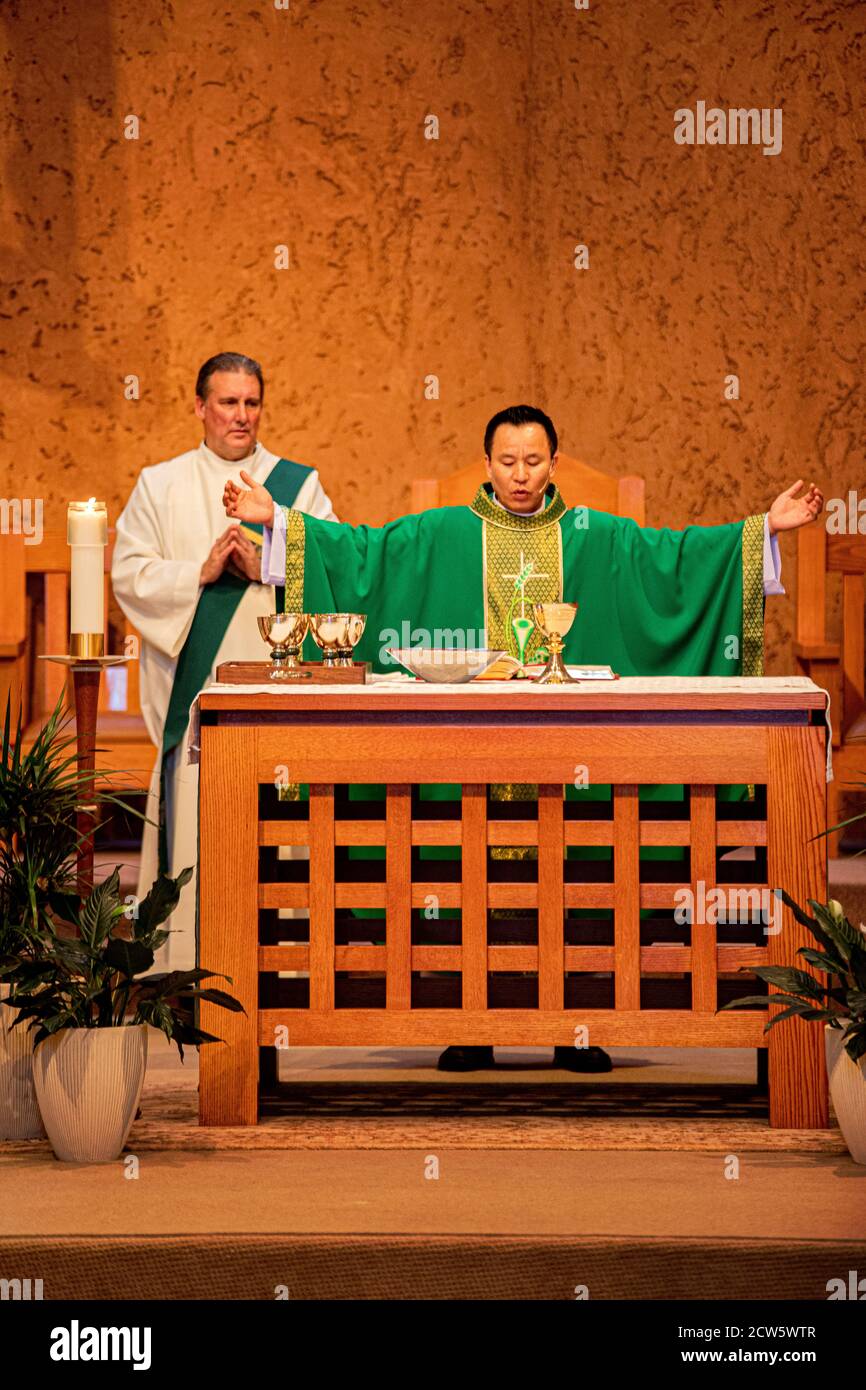 A robed deacon and an Asian American priest celebrate mass at the altar of a Southern California Catholic church. Note goblets for sacramental wine. Stock Photo