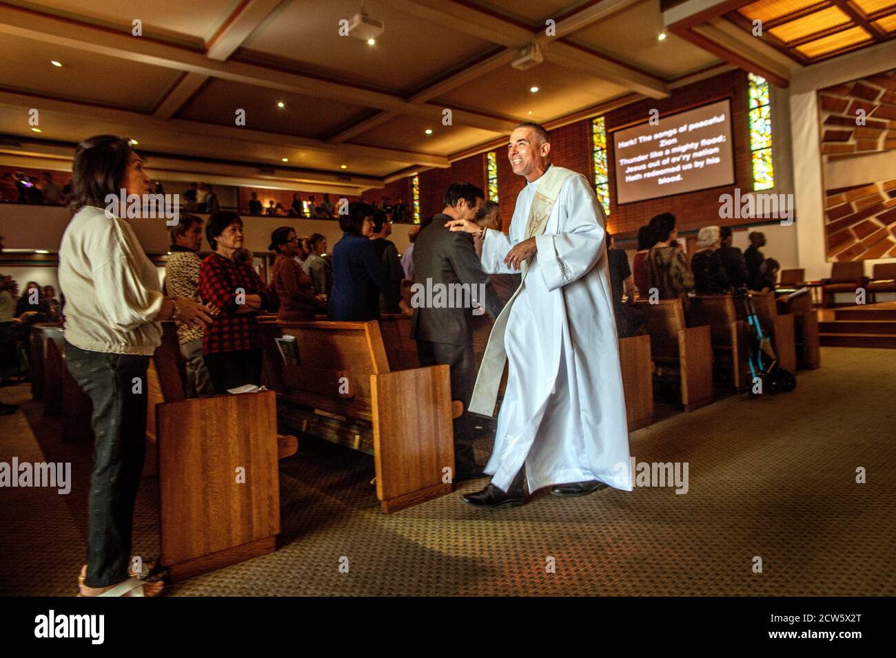 A friendly deacon welcomes an arriving parishioner at mass in a Southern California Catholic church. Stock Photo