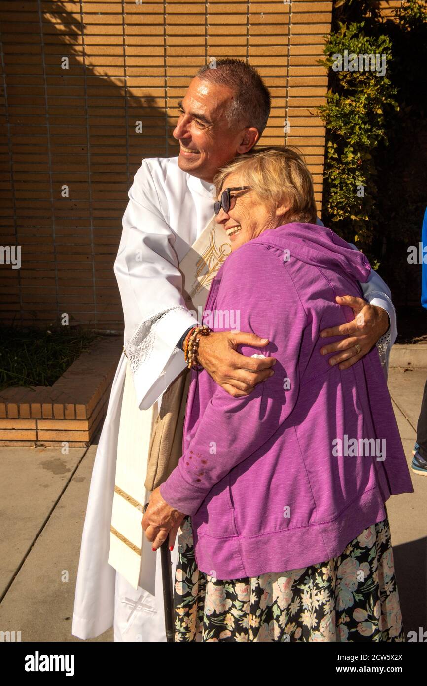 After mass, the deacon of a Southern California Catholic church hugs a parishioner in the church outdoor yard. Stock Photo
