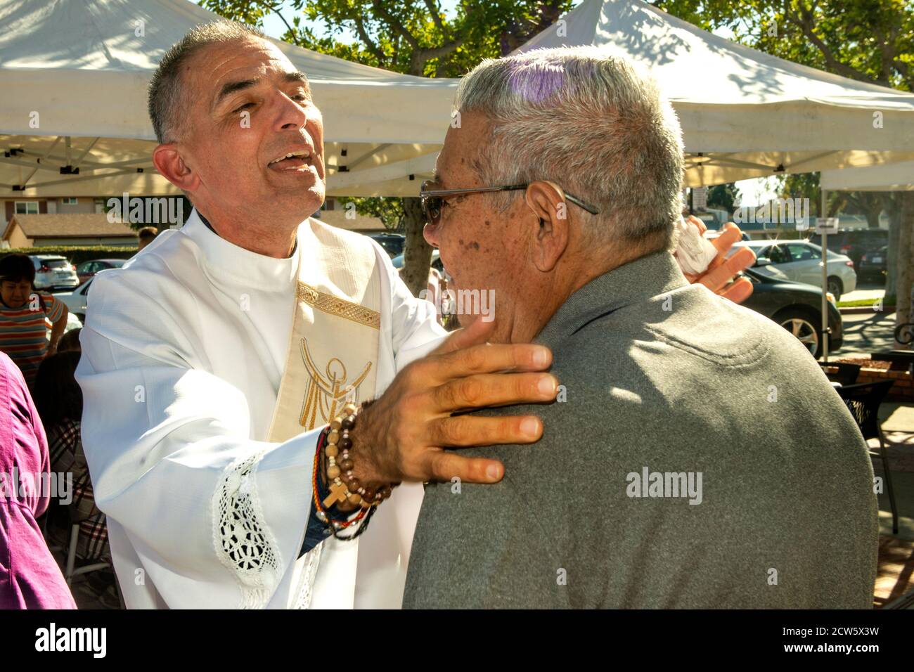 After mass, the deacon of a Southern California Catholic church embraces a parishioner in the church outdoor yard. Stock Photo
