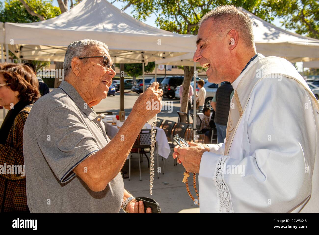 After mass, the deacon of a Southern California Catholic church greets a parishioner who shows him his rosary in the church outdoor yard. Stock Photo