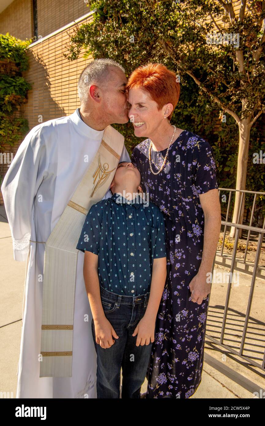 After mass, the deacon of a Southern California Catholic church  poses with a female parishioner and her son in the church outdoor yard. Stock Photo