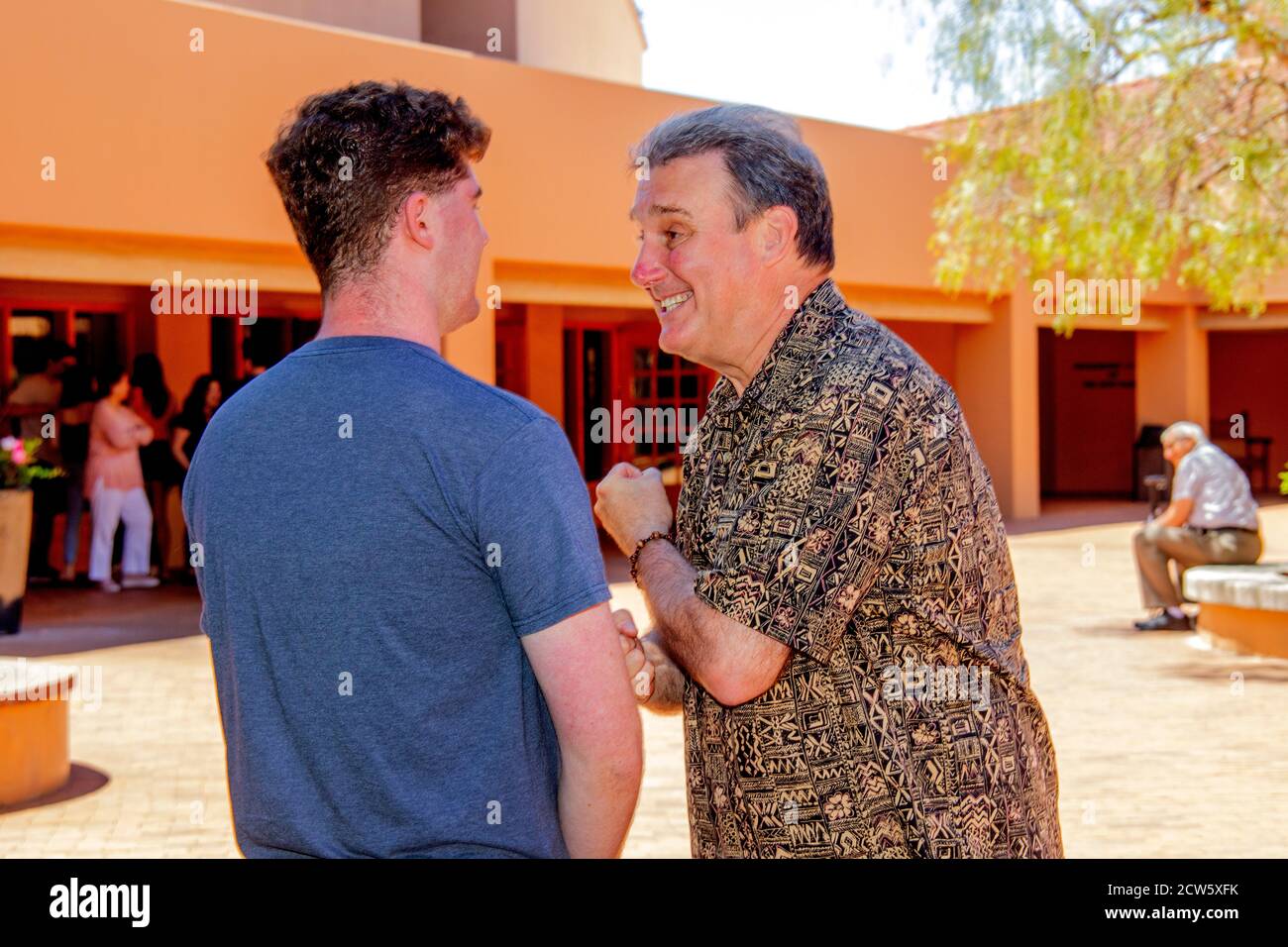 The deacon of a Southern California Catholic church greets a young adult parishioner after mass in the church courtyard. Stock Photo