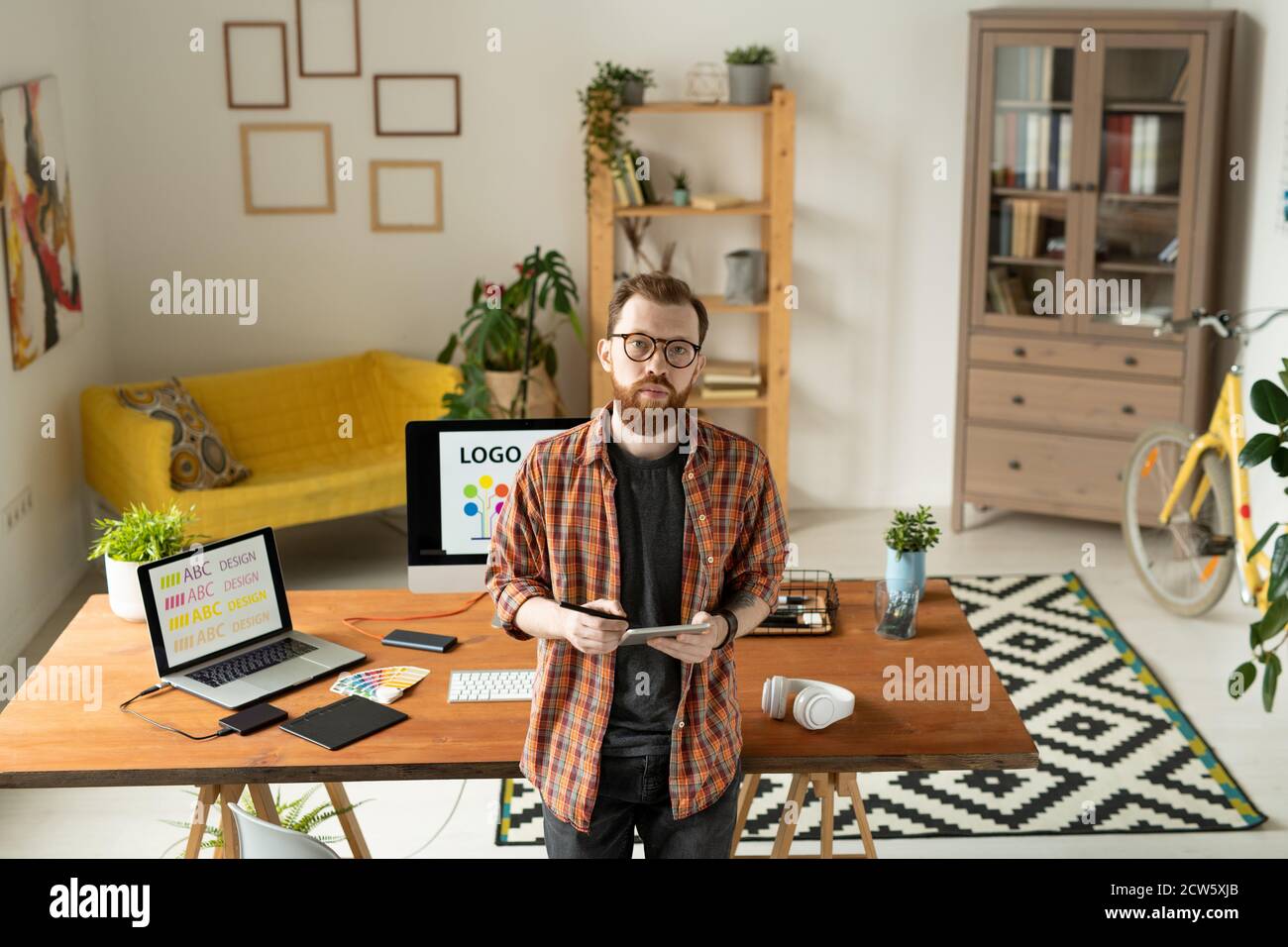 Serious creative designer standing by table with computer monitor on background Stock Photo