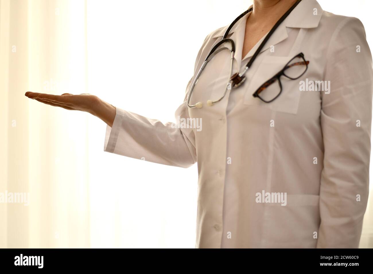The doctor in a white robe stands with her arm outstretched and an empty palm showing anything.  Stock Photo