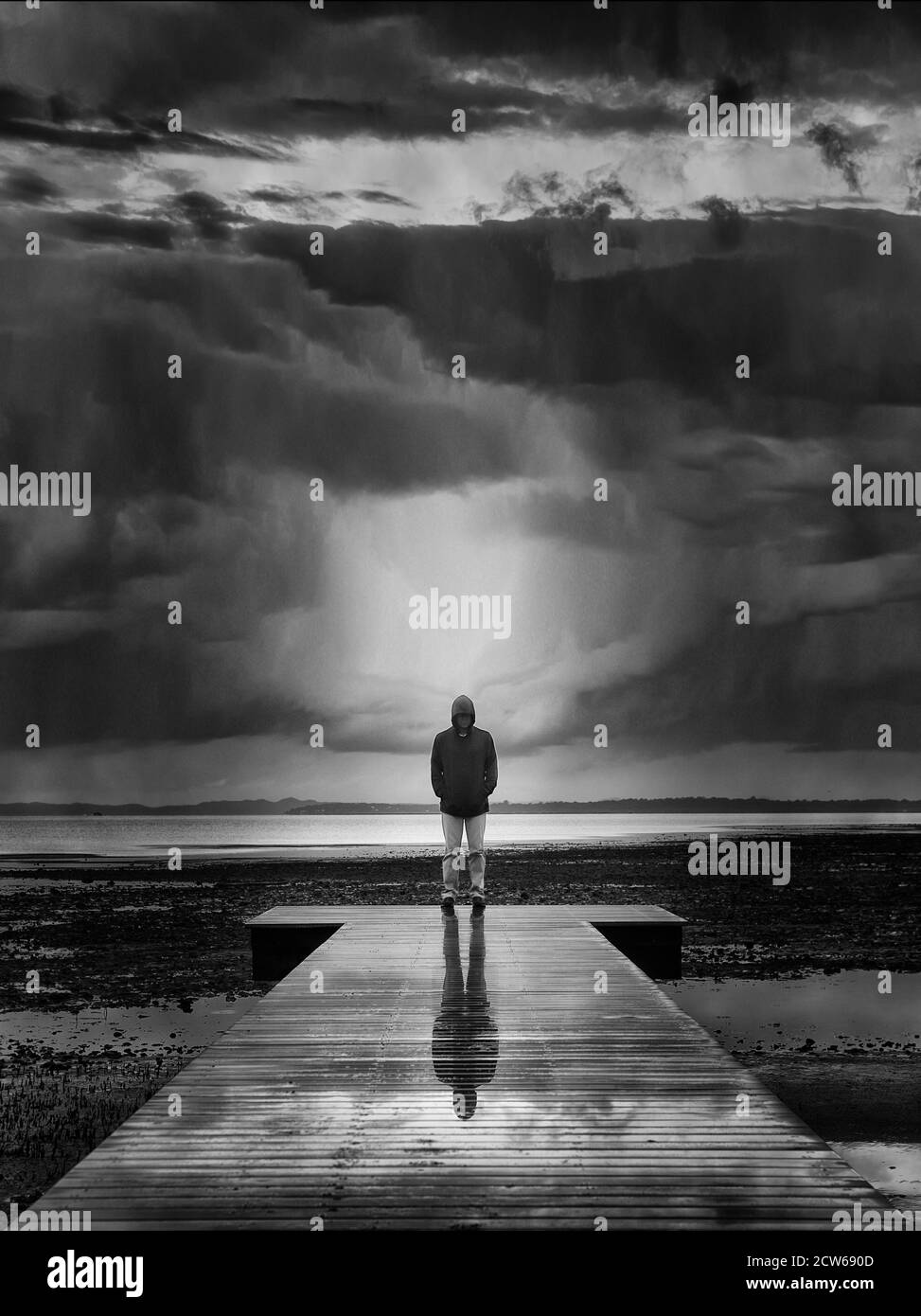 A black and white fine art image of a single male standing on a pier at sunset with a brewing thunderstorm out to sea at Cleveland Point, Australia Stock Photo