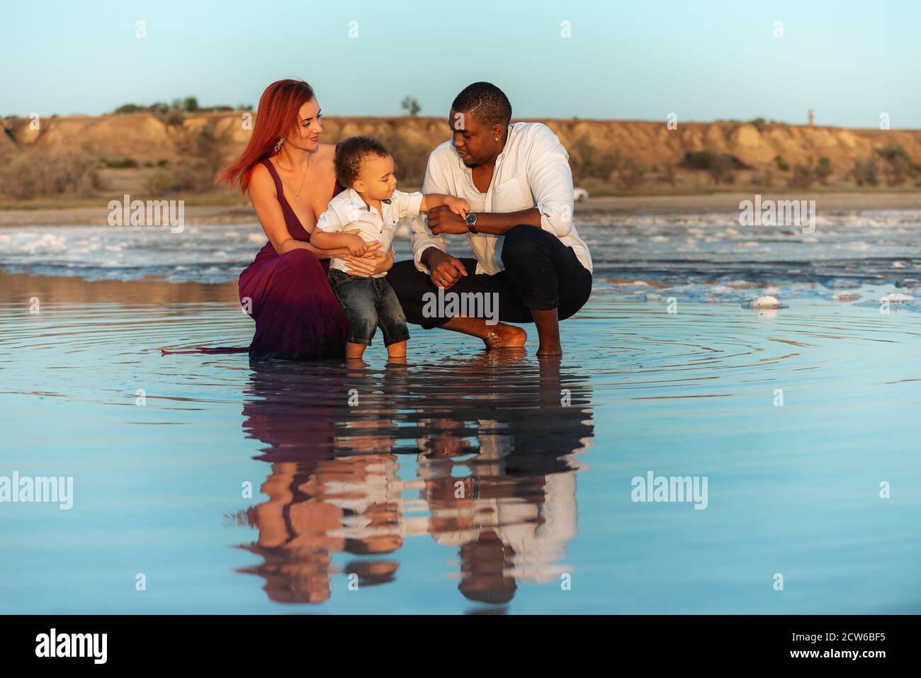 Loving mixed raced family together, parents with their little baby at sunset. Happy harmonious family outdoors concept Stock Photo