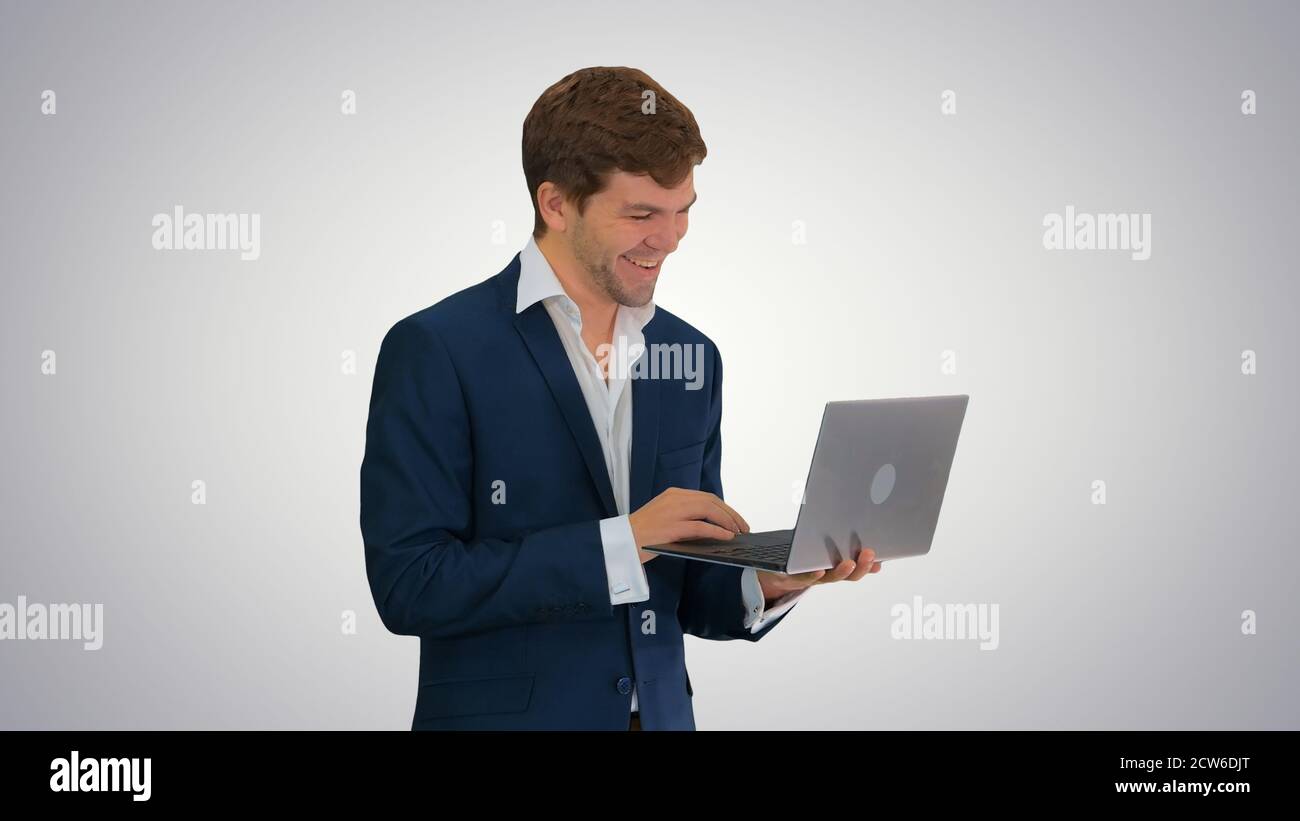 Smiling young businessman using laptop while standing on gradien Stock Photo