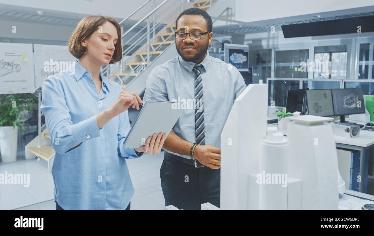 In Architectural Bureau: Architect and Engineer Talking, Working on a Building Complex Prototype Project, Using City Model and Computers Running 3D Stock Photo