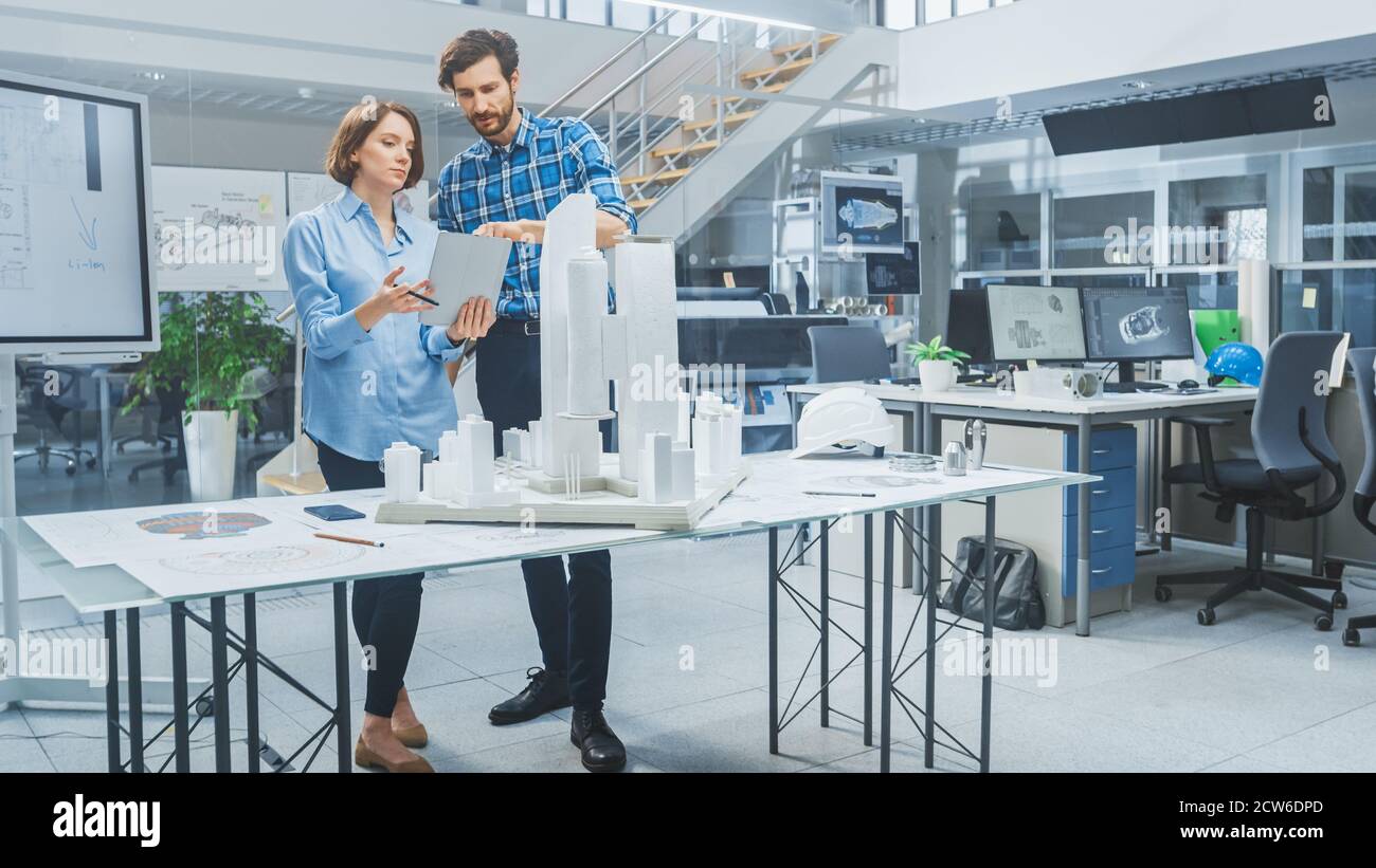 In Architectural Bureau: Architect and Engineer Talking, Using Digital Tablet Computer, Working on a Building Complex Prototype Project, Using City Stock Photo