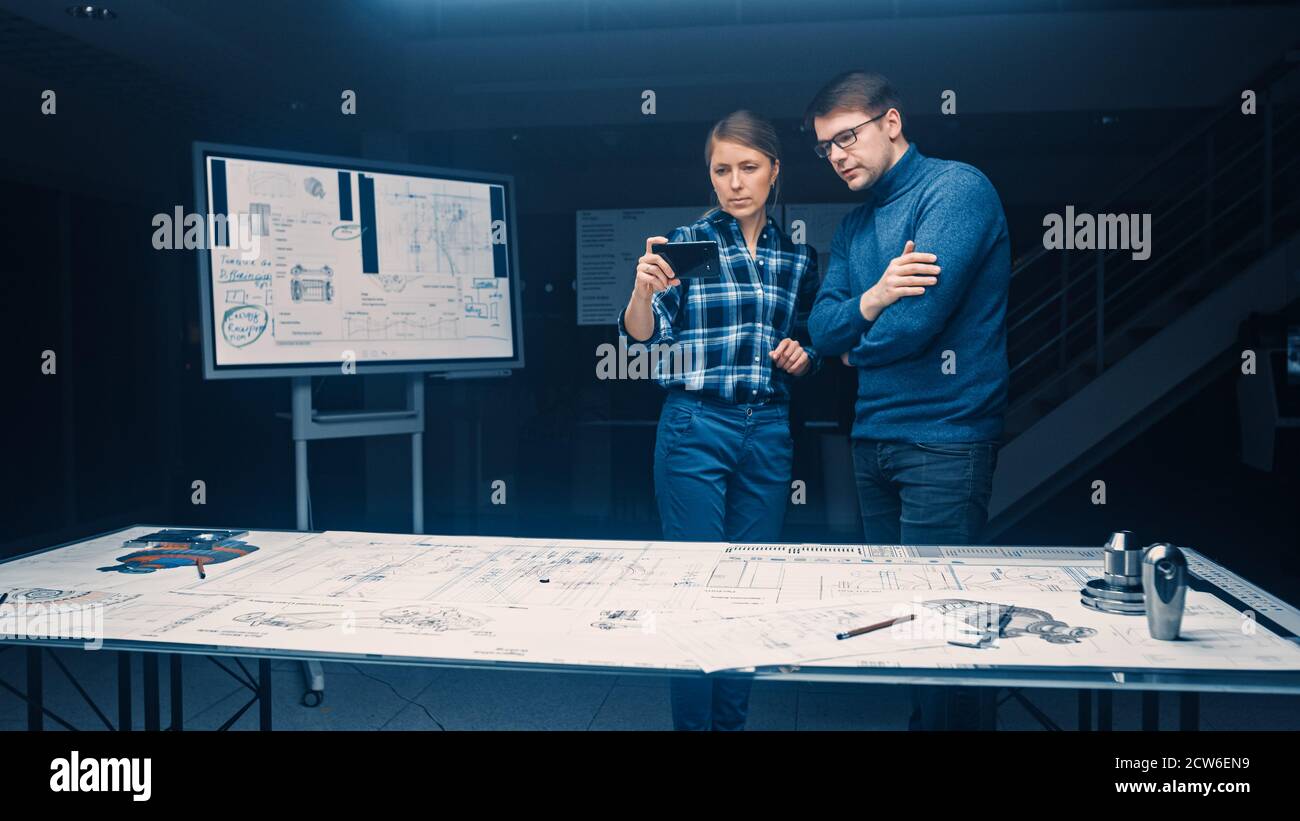 Two Young Software Development Engineers Talk and Use Smartphone with Augmented Reality for Reading and Interacting with Car and Engine Concept Stock Photo