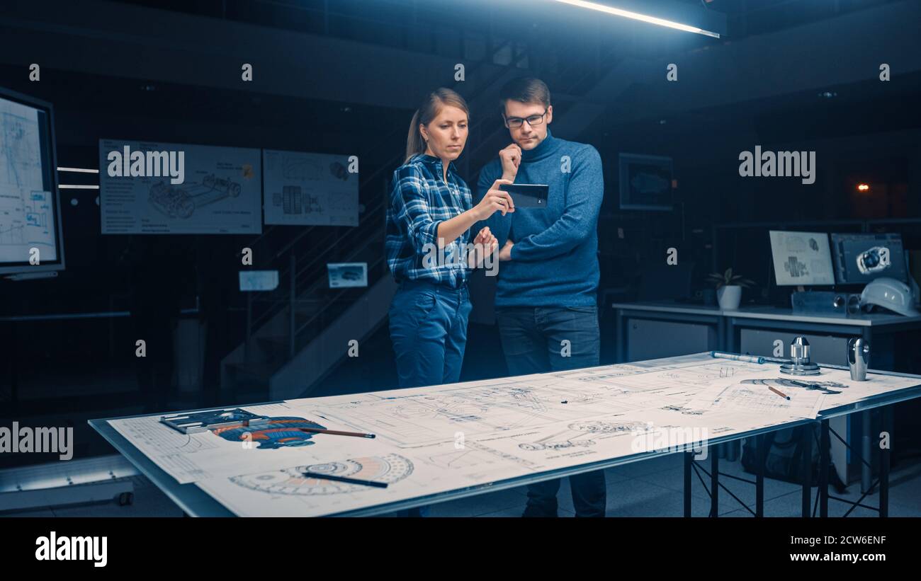 Two Young Software Development Engineers Talk and Use Smartphone with Augmented Reality for Reading and Interacting with Car and Engine Concept Stock Photo