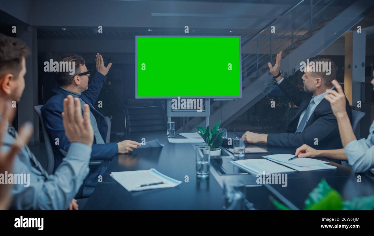 Late at Night In Corporate Meeting Room: Board of Directors, Executives and Businesspeople Sitting at Negotiations Table, Talking and Using Green Mock Stock Photo
