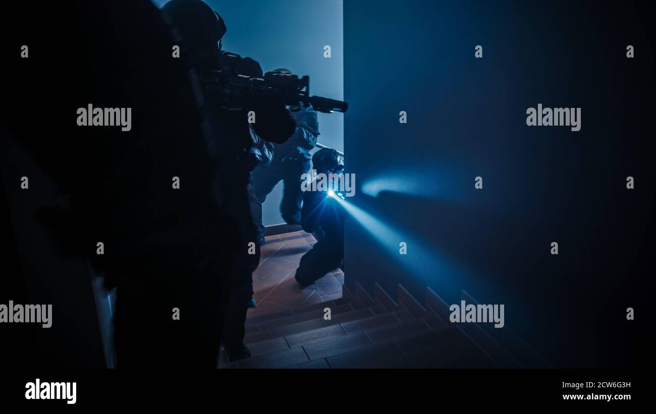 Masked Squad of Armed SWAT Police Officers Move Up the Stairs in a Corridor of an Office Building. Soldiers with Rifles and Flashlights Move Forwards Stock Photo