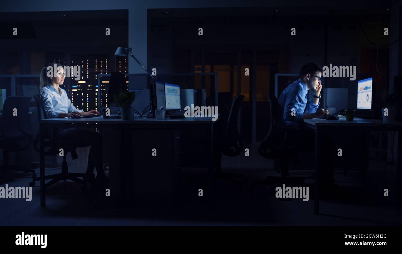 Working Late at Night in the Office: Businesspeople Use Desktop Computer, Analyzing, Using Documents, Solving Problems, Finishing Important Project Stock Photo