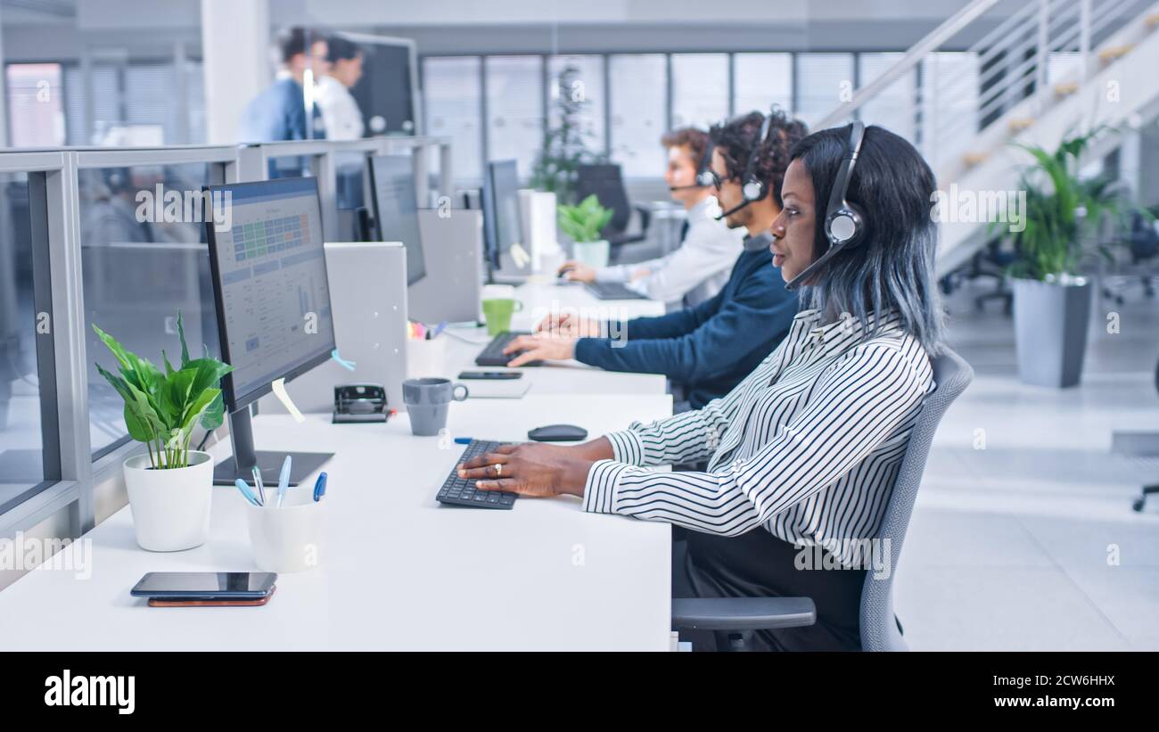 Team of Handsome and Beautiful Diverse Multicultural Customer Service Operators Working at a Busy Modern Call Center with Specialists Wearing Headsets Stock Photo