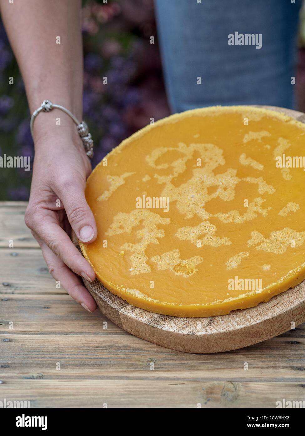 Woman holding yellow rounded piece of melted beeswax on wooden table. Copy space Stock Photo