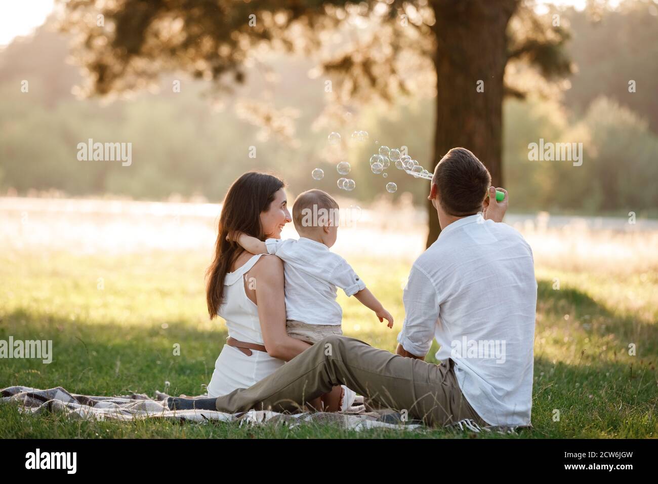 father, mother and son blow soap bubbles in the park together on a sunny summer day. happy
