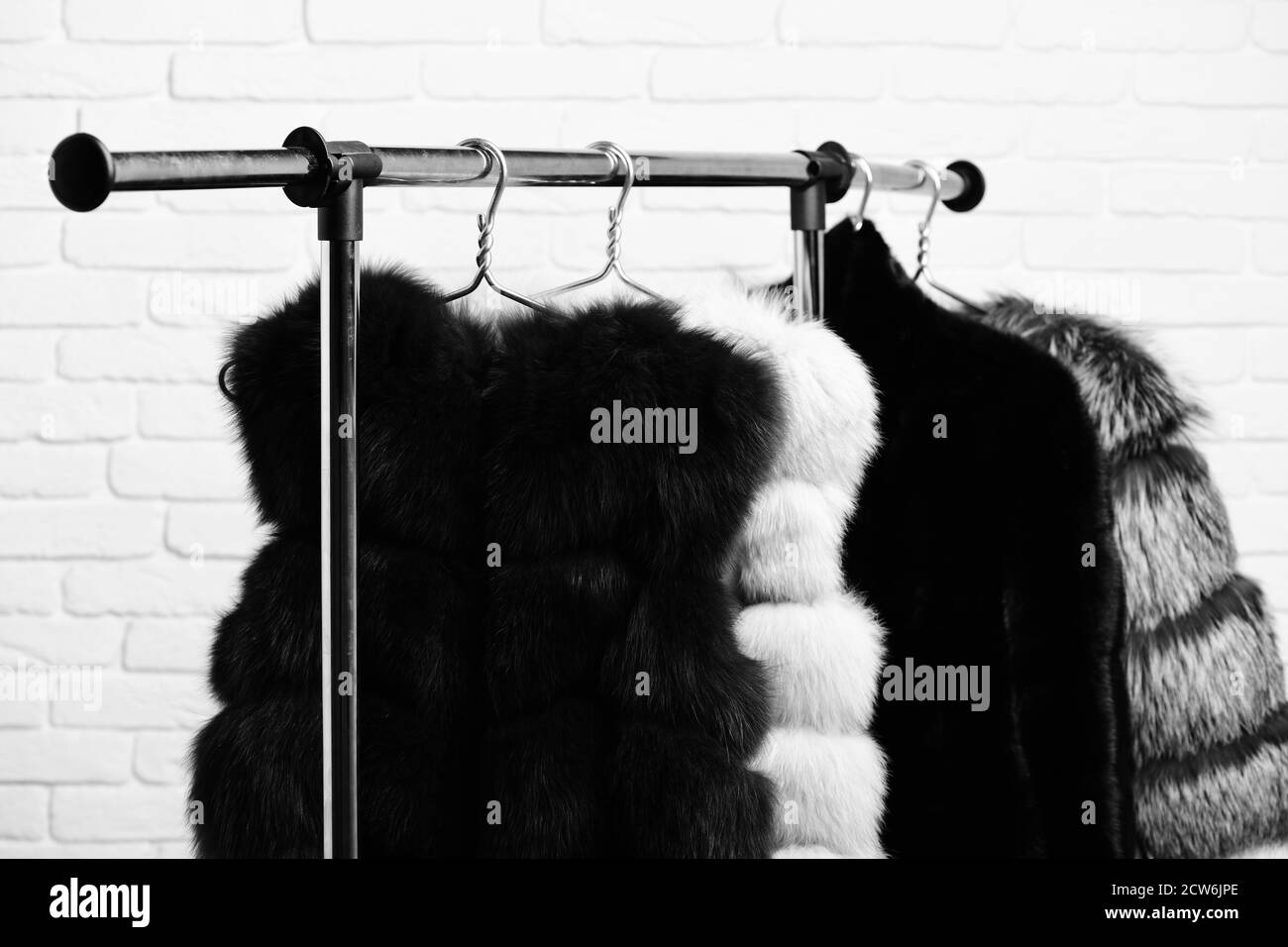 fashionable luxurious waist coats of fur hanging on rack on golden hangers on brick wall studio