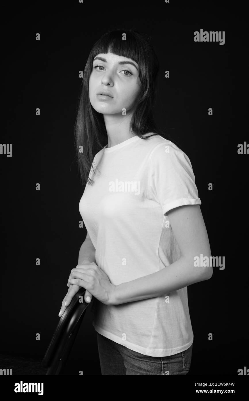 Studio portrait of a pretty brunette woman in a white blank t-shirt, against a plain black background, looking at camera Stock Photo