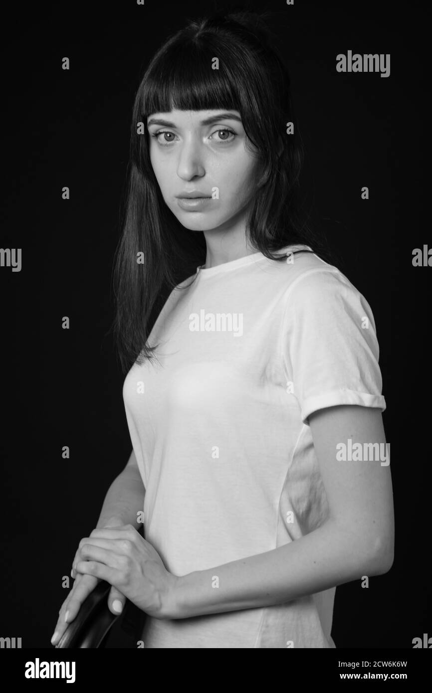 Studio portrait of a pretty brunette woman in a white blank t-shirt, against a plain black background, seriouly looking at camera Stock Photo