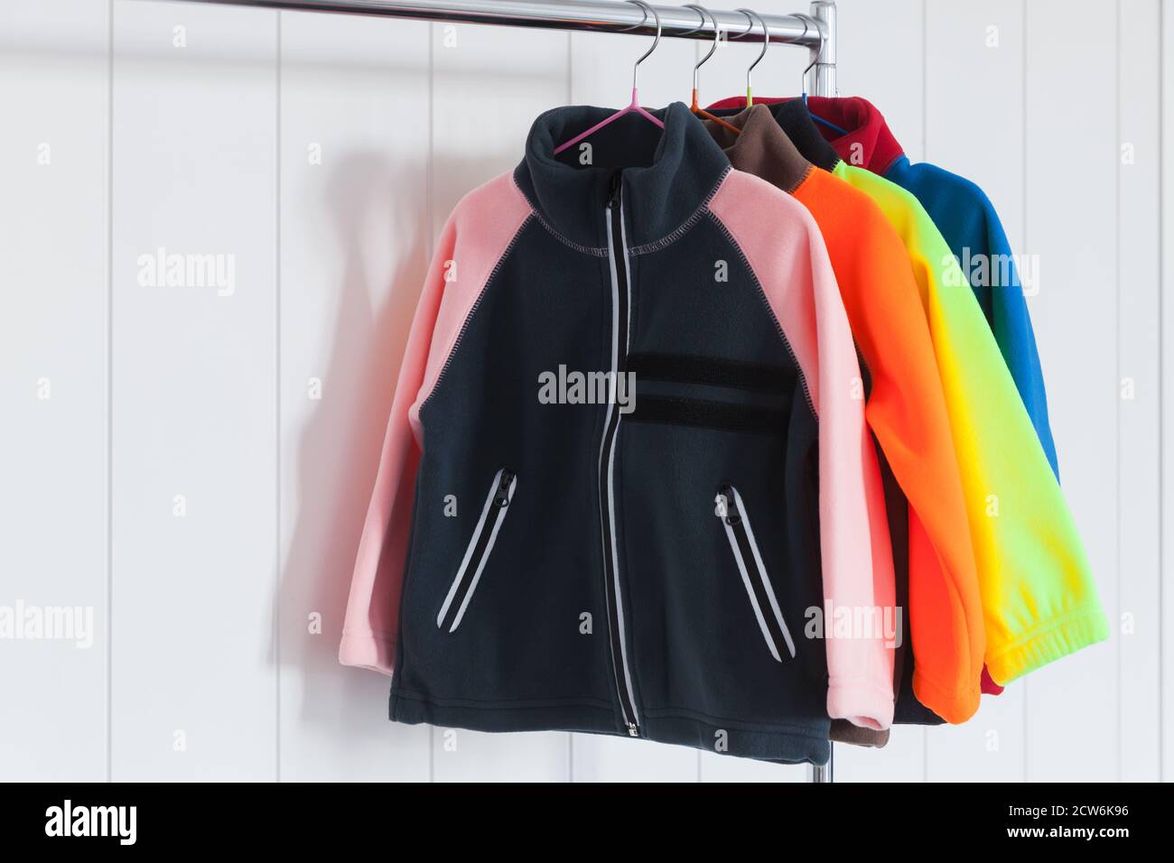 Colorful fleece jackets are hanging on hangers near white wall Stock Photo